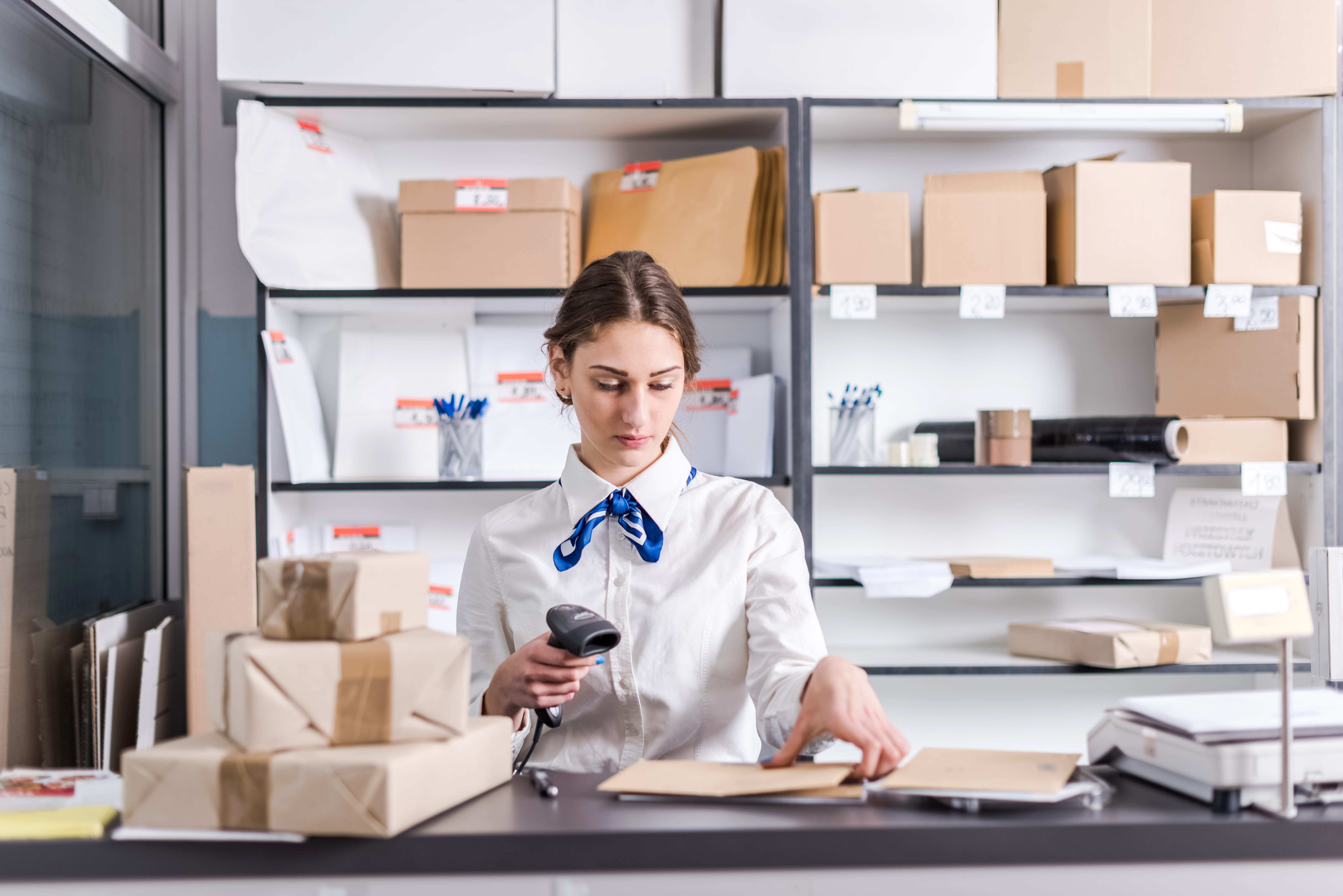 Woman working at a staffed post office counter handling mail and packages
