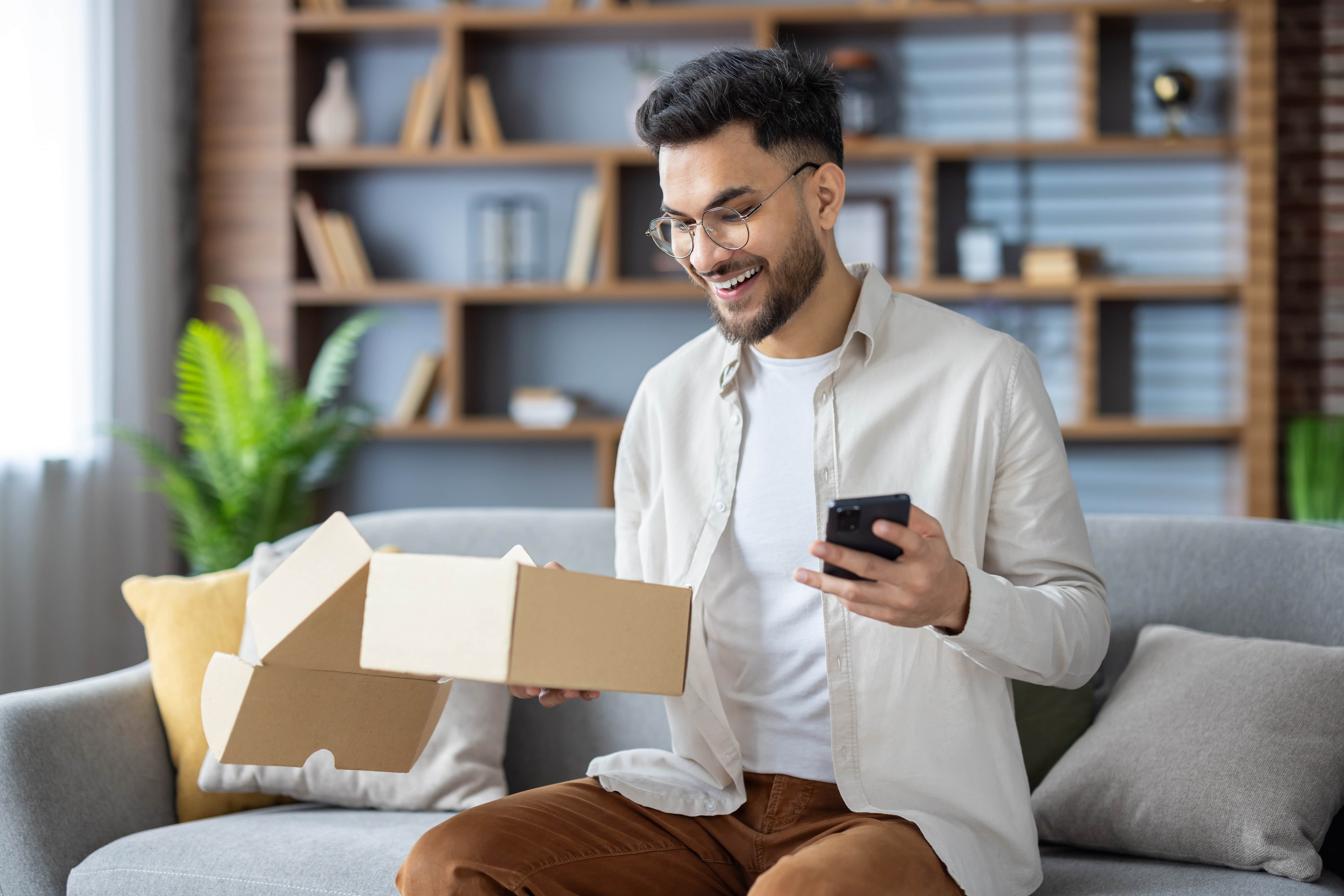 man with glasses sitting on a couch holding a small brown box